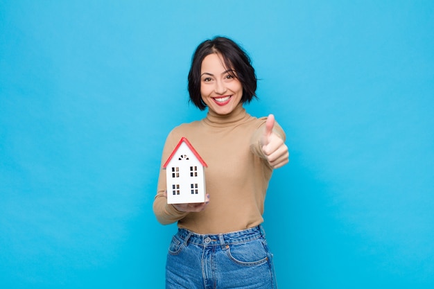 Mujer bonita joven que se siente orgullosa, despreocupada, segura y feliz, sonriendo positivamente con los pulgares arriba con una modelo de casa