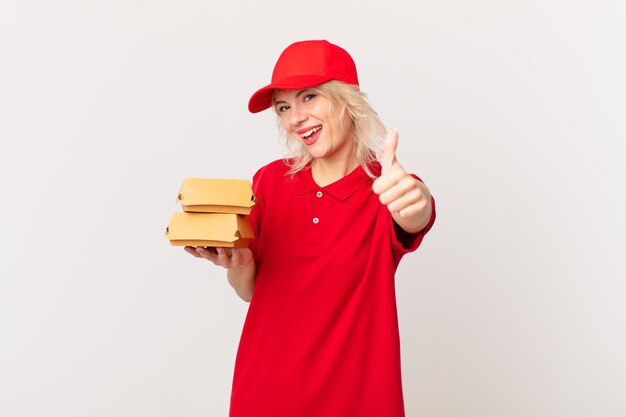 Mujer bonita joven que se siente orgullosa, sonriendo positivamente con los pulgares hacia arriba. concepto de entrega de hamburguesas