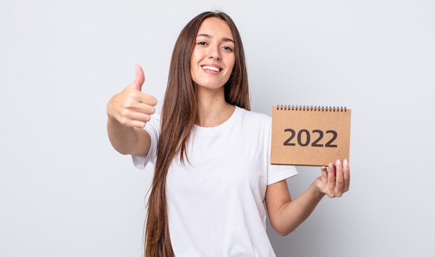 Foto mujer bonita joven que se siente orgullosa, sonriendo positivamente con los pulgares hacia arriba. concepto de planificador 2022