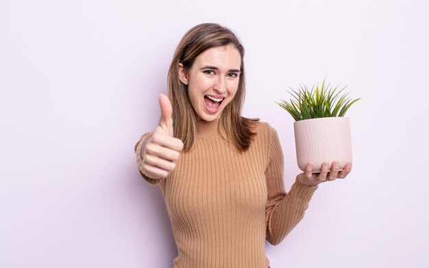 Mujer bonita joven que se siente orgullosa, sonriendo positivamente con los pulgares hacia arriba. concepto de planta