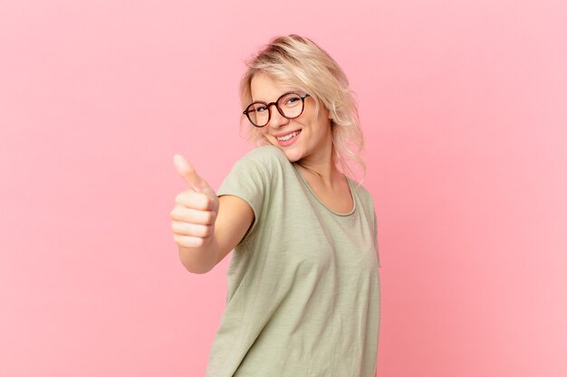 Mujer bonita joven que se siente orgullosa, sonriendo positivamente con los pulgares hacia arriba