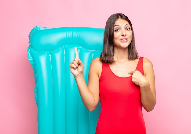 Mujer bonita joven que se siente orgullosa y sorprendida, apuntando a sí misma con confianza, sintiéndose como el número uno exitoso