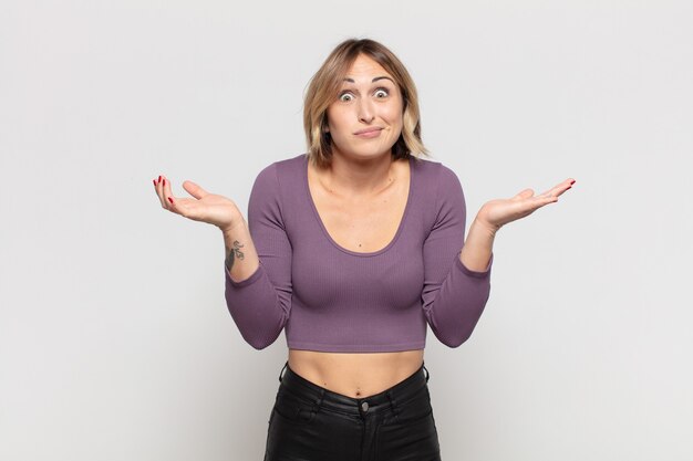 Foto mujer bonita joven que se siente perpleja y confundida, dudando, ponderando o eligiendo diferentes opciones con expresión divertida