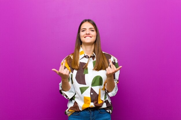 Mujer bonita joven que se siente provocativa, agresiva y obscena, moviendo el dedo medio, con una actitud rebelde contra el fondo púrpura.