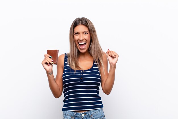 Mujer bonita joven que se siente sorprendida, emocionada y feliz, riendo y celebrando el éxito, diciendo ¡guau! con una billetera de cuero.