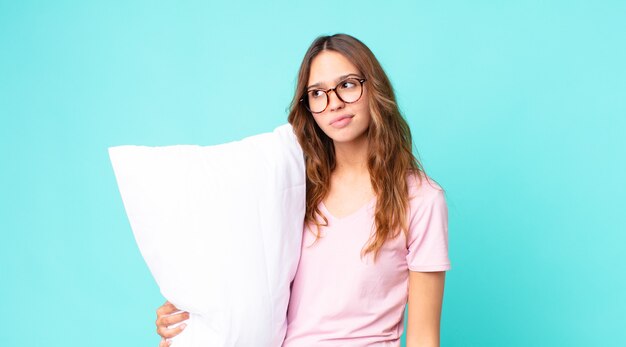 Mujer bonita joven que se siente triste, molesta o enojada y mirando hacia un lado en pijama y sosteniendo una almohada