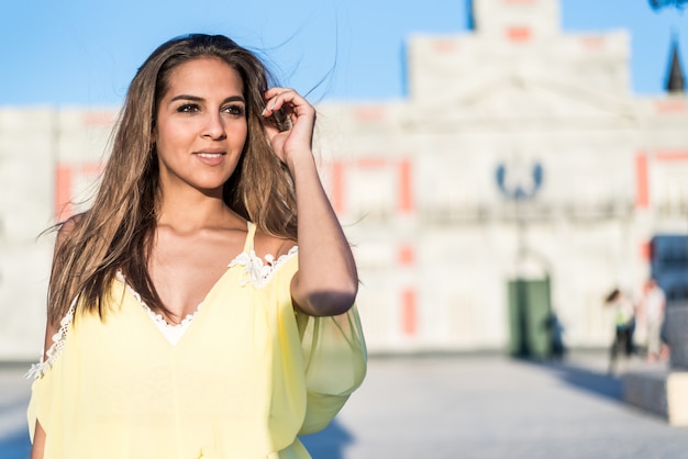 Mujer bonita joven que sonríe aislada cerca al aire libre con un vestido amarillo