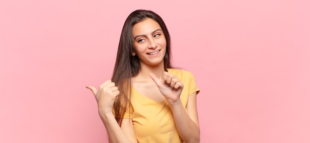 Mujer bonita joven que sonríe alegremente y casualmente apuntando al espacio de la copia en el lado, sintiéndose feliz y satisfecho