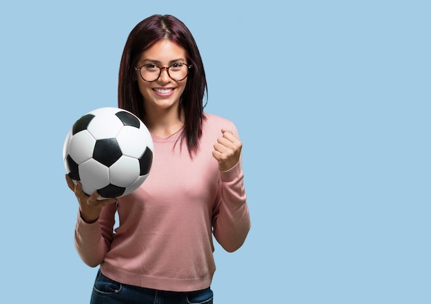 Mujer bonita joven que sonríe y feliz, sosteniendo un balón de fútbol, actitud competitiva