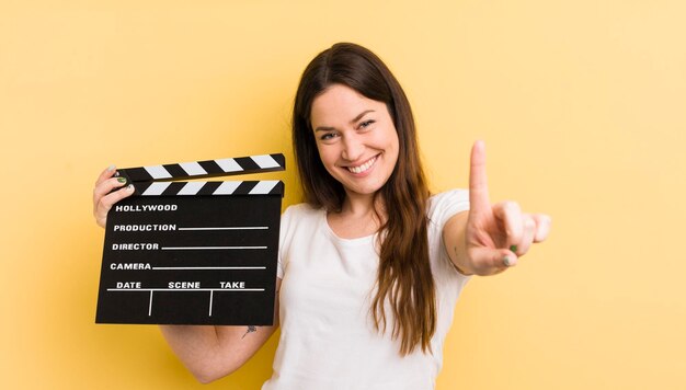 Mujer bonita joven que sonríe con orgullo y confianza haciendo el concepto de badajo de cine número uno