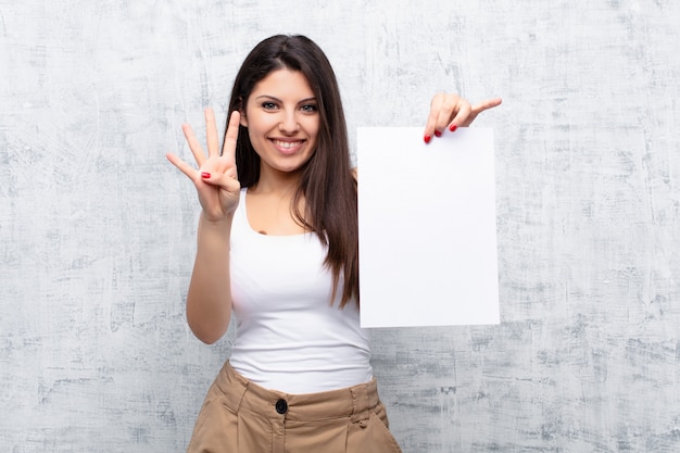 Mujer bonita joven que sostiene una hoja de papel contra la pared de cemento del grunge