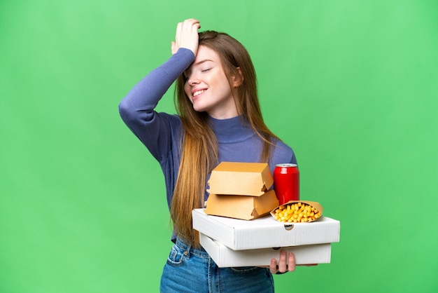 Una mujer bonita joven que sostiene pizzas y hamburguesas sobre un fondo de clave de croma aislado se ha dado cuenta de algo y tiene la intención de encontrar la solución