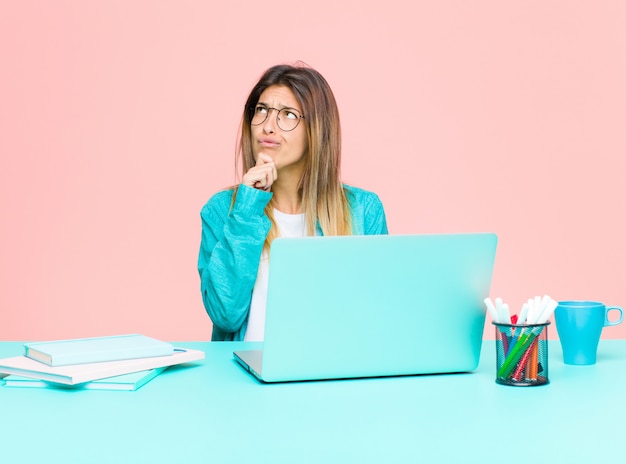 Mujer bonita joven que trabaja con una computadora portátil pensando, sintiéndose dudosa y confundida, con diferentes opciones, preguntándose qué decisión tomar