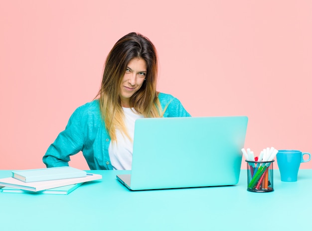 Mujer bonita joven que trabaja con una computadora portátil que parece orgullosa, confiada, fresca, descarada y arrogante, sonriente, sintiéndose exitosa