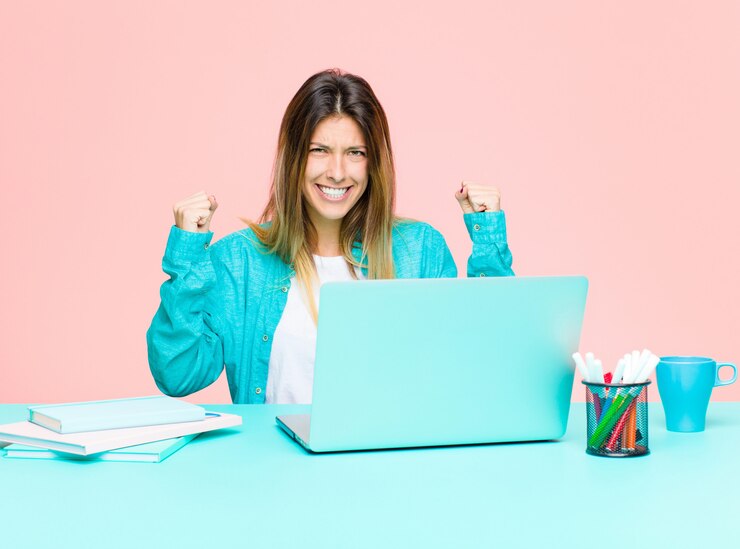 Foto mujer bonita joven que trabaja con una computadora portátil sintiéndose feliz, sorprendida y orgullosa, gritando y celebrando el éxito con una gran sonrisa