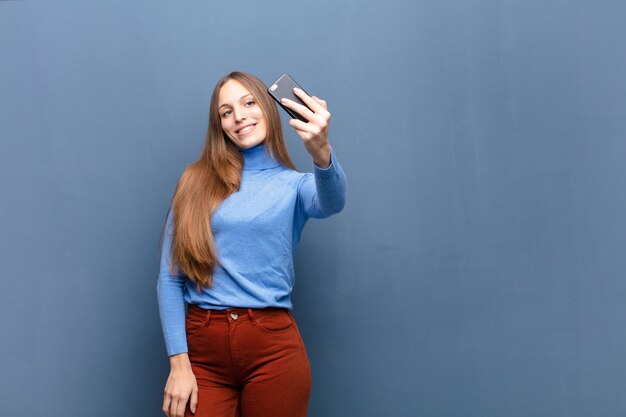 Mujer bonita joven que usa un teléfono inteligente contra la pared azul con un espacio de copia