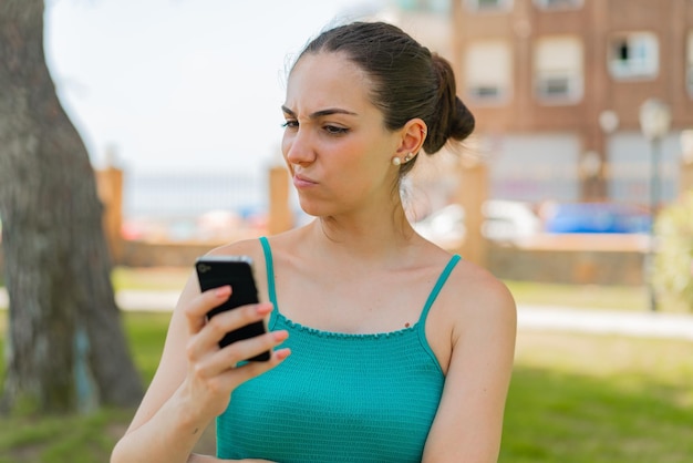 Mujer bonita joven que usa el teléfono móvil al aire libre con expresión triste