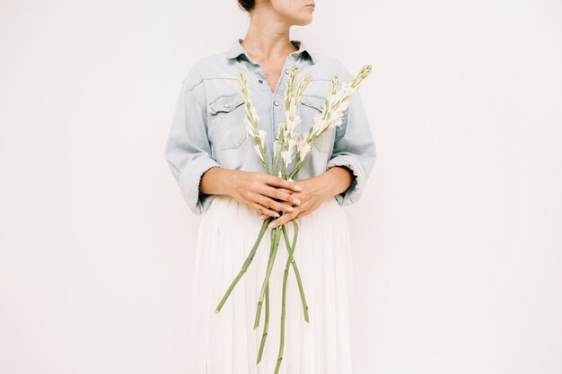 Mujer bonita joven con ramo de flores blancas cerca de la pared blanca