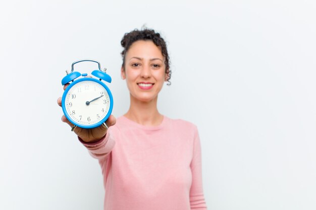 Mujer bonita joven con un reloj de alarma contra blanco