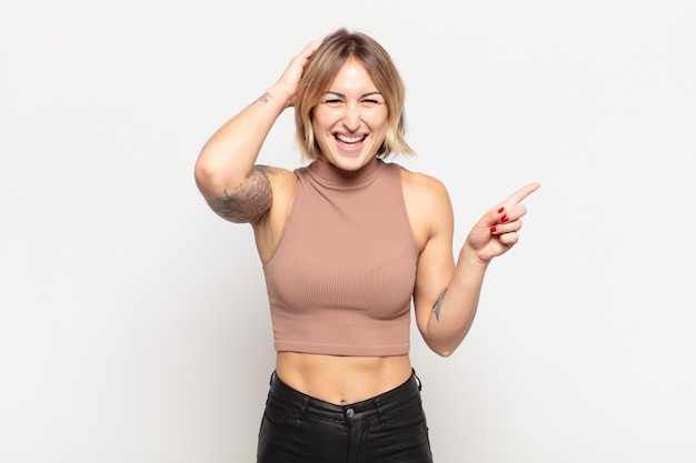 Mujer bonita joven riendo, luciendo feliz, positiva y sorprendida, dándose cuenta de una gran idea apuntando al espacio de copia lateral