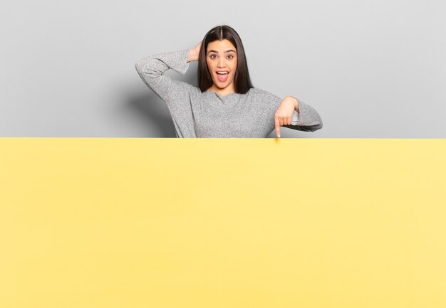 Mujer bonita joven riendo, luciendo feliz, positiva y sorprendida, dándose cuenta de una gran idea apuntando al espacio lateral de la copia.