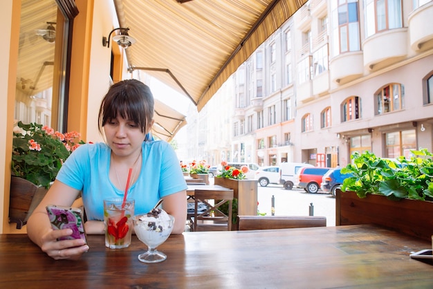 Mujer bonita joven sentada en un café usando su teléfono y bebiendo bebidas frías en el día de verano