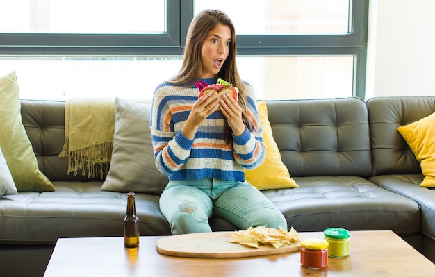 Foto mujer bonita joven sentada en un sofá de cuero comiendo