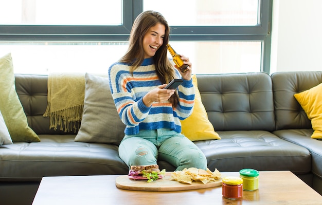 Foto mujer bonita joven sentada en un sofá de cuero comiendo