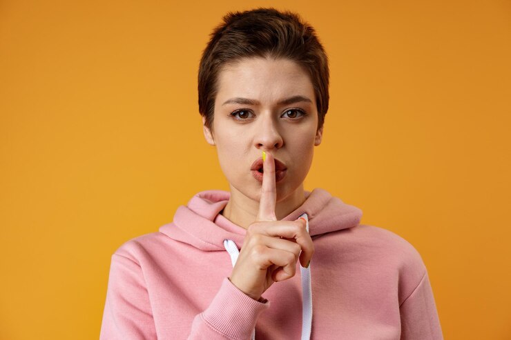 Foto mujer bonita joven seria que muestra gesto de silencio sobre fondo amarillo