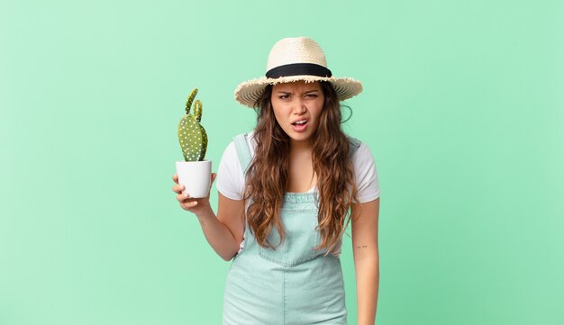 Mujer bonita joven sintiéndose desconcertado y confundido y sosteniendo un cactus