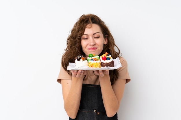 Foto mujer bonita joven sobre aislado sosteniendo mini pasteles disfrutando el olor de ellos