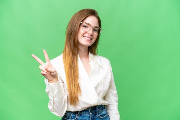 Mujer bonita joven sobre fondo clave de croma aislado sonriendo y mostrando el signo de la victoria