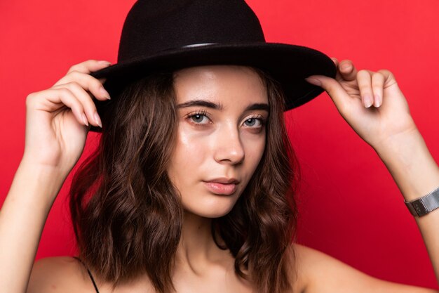 Mujer bonita joven con sombrero de ala ancha aislado sobre pared roja