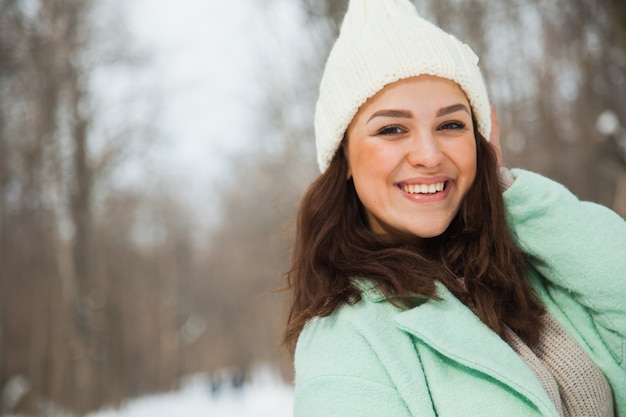 Mujer bonita joven con sombrero tejido a mano de sonrisa feliz n blanco. Día de invierno con nieve, clima helado.