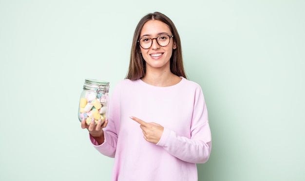 Mujer bonita joven sonriendo alegremente, sintiéndose feliz y apuntando hacia un lado. concepto de caramelos de gelatina