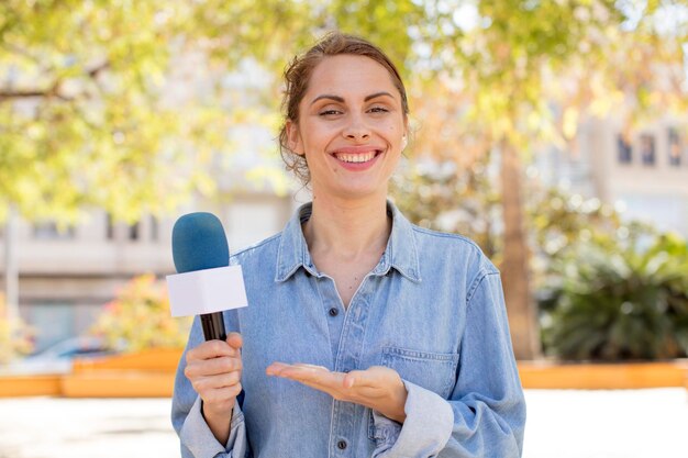 mujer bonita joven sonriendo alegremente sintiéndose feliz y mostrando un presentador de concepto y concepto de micrófono