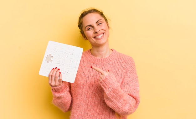 Mujer bonita joven sonriendo alegremente sintiéndose feliz y señalando el concepto de rompecabezas lateral