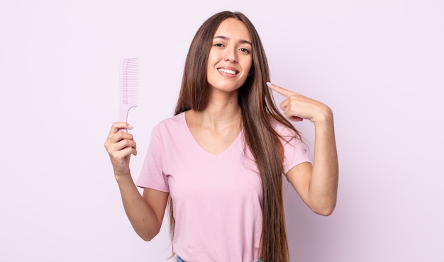 Mujer bonita joven sonriendo con confianza apuntando a su propia amplia sonrisa. concepto de peine de pelo