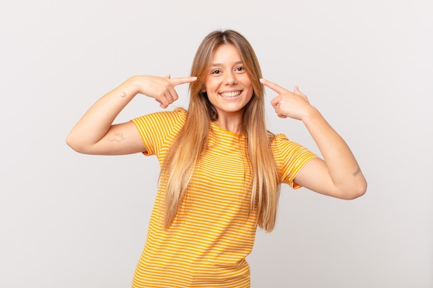 Mujer bonita joven sonriendo con confianza apuntando a su propia amplia sonrisa