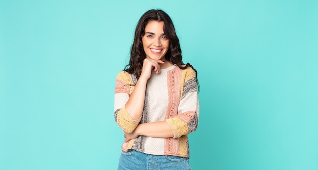 Foto mujer bonita joven sonriendo, disfrutando de la vida, sintiéndose feliz, amigable, satisfecho y despreocupado con la mano en la barbilla