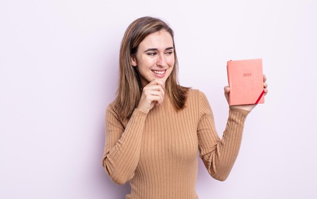 Mujer bonita joven sonriendo con una expresión feliz y segura con la mano en la barbilla. concepto de agenda