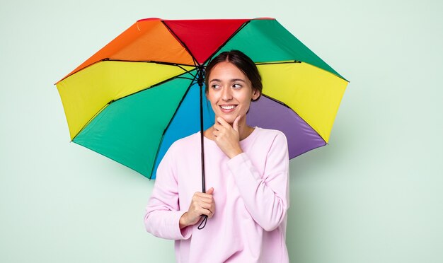 Mujer bonita joven sonriendo con una expresión feliz y segura con la mano en la barbilla. concepto de paraguas