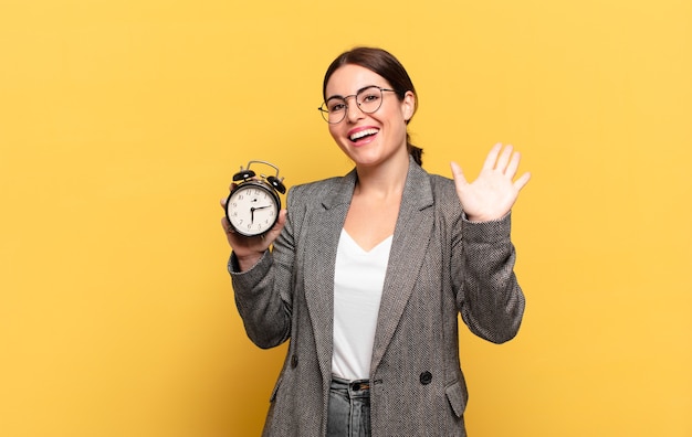 Mujer bonita joven sonriendo feliz y alegremente, saludando con la mano, dándote la bienvenida y saludándote, o diciendo adiós