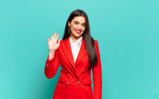 Mujer bonita joven sonriendo feliz y alegremente, saludando con la mano, dándote la bienvenida y saludándote, o diciéndote adiós. concepto de negocio