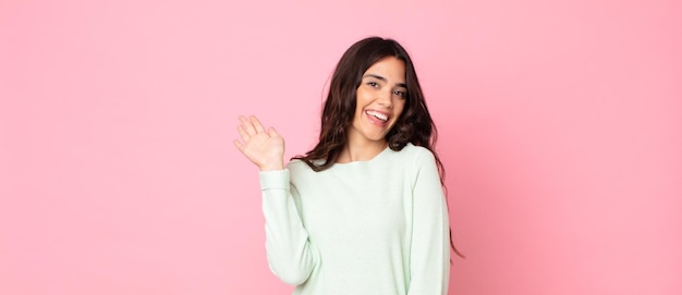 Mujer bonita joven sonriendo feliz y alegremente, saludando con la mano, dándote la bienvenida y saludándote, o diciéndote adiós