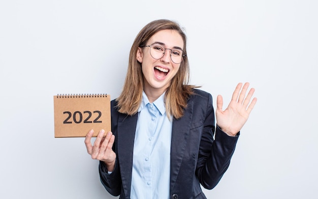 Mujer bonita joven sonriendo felizmente agitando la mano dándole la bienvenida y saludando el concepto de calendario