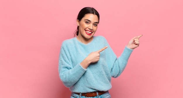 Mujer bonita joven sonriendo felizmente y apuntando hacia un lado y hacia arriba con ambas manos mostrando el objeto en el espacio de la copia