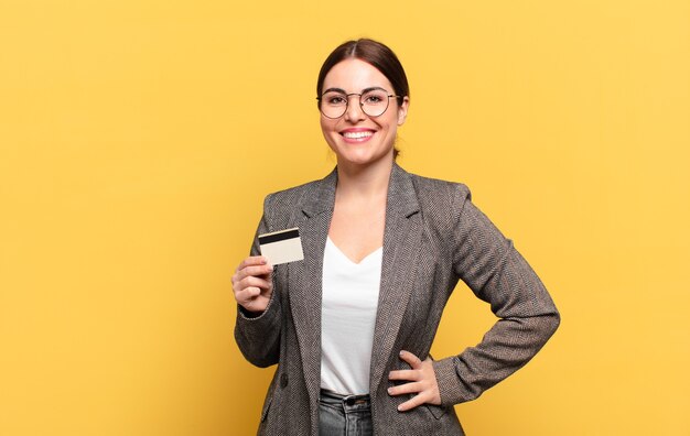 Mujer bonita joven sonriendo felizmente con una mano en la cadera y actitud confiada, positiva, orgullosa y amistosa