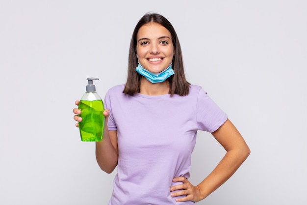 Mujer bonita joven sonriendo felizmente con una mano en la cadera y actitud confiada, positiva, orgullosa y amistosa