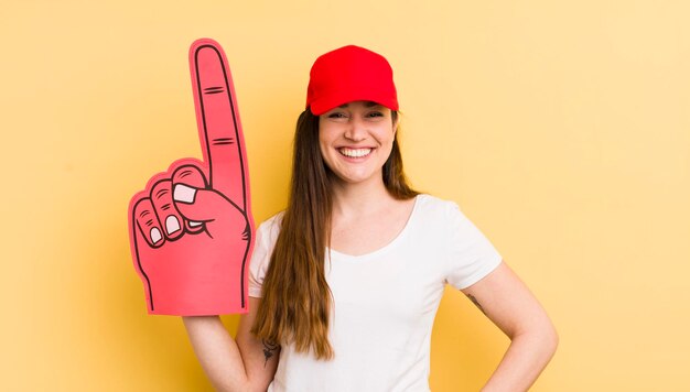 Mujer bonita joven sonriendo felizmente con una mano en la cadera y el concepto de mano número uno confiado